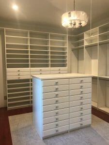 Bright custom white walk-in closet featuring a chandelier, large island drawers, and open shelving for clothing and shoes