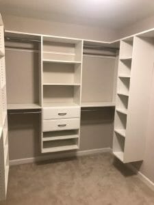 Minimalist custom white walk-in closet featuring drawers, hanging rods, and built-in corner shelving for efficient storage