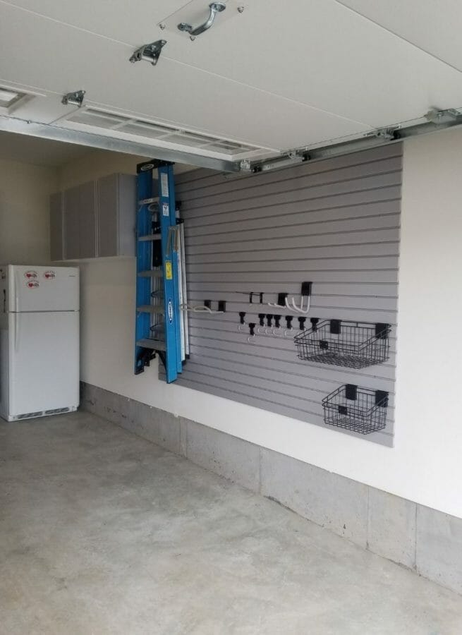 Wall-mounted slatwall garage storage system with hanging hooks and wire baskets for tools and equipment.