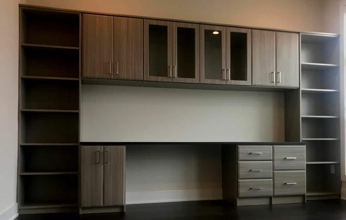 Modern home office design with gray wood built-in desk, glass cabinet doors, and open shelving for storage efficiency.
