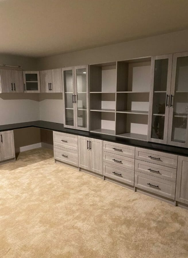 Spacious built-in home office with light wood cabinets, drawers, and glass display shelving for an elegant workspace.