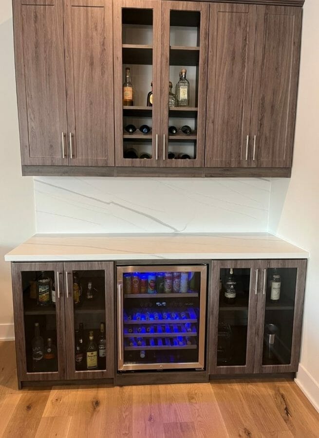 Modern home bar with dark wood cabinets, glass doors, built-in wine storage, and beverage cooler with LED lighting.