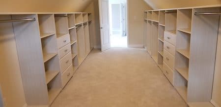 Long walk-in closet with matching built-in shelving, drawers, and hanging rods on both sides, finished with carpet and a doorway at the end.