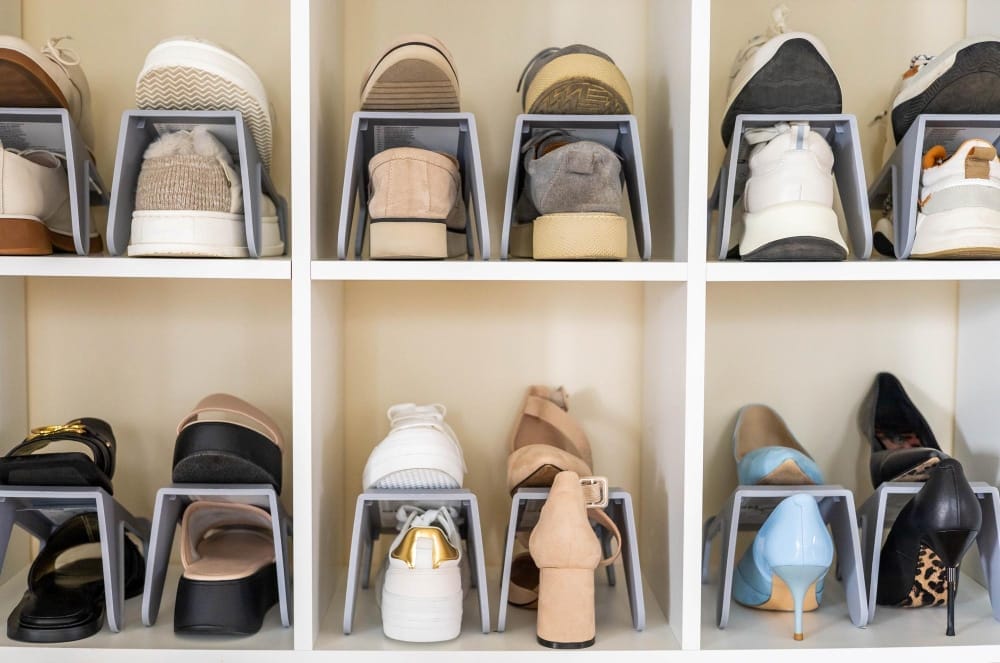 Organized shoe storage in a walk-in closet with cubby shelves and gray shoe racks holding sneakers, heels, and flats.