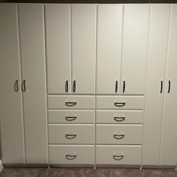 Closed view of white wardrobe closet with multiple drawers and tall cabinets, providing concealed and stylish clothing storage.